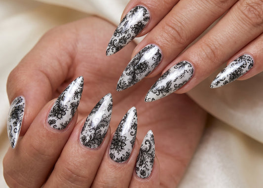 Hand with black and white floral nail design on a neutral background