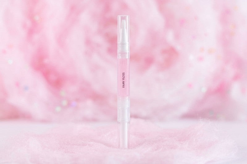 White fairy floss scented cuticle oil pen with pink text on a soft pink and white cloud background. The best scented cuticle oil range from unicorn lab
