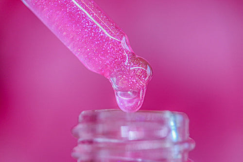 Pink liquid being dripped from a dropper into a clear container against a pink background