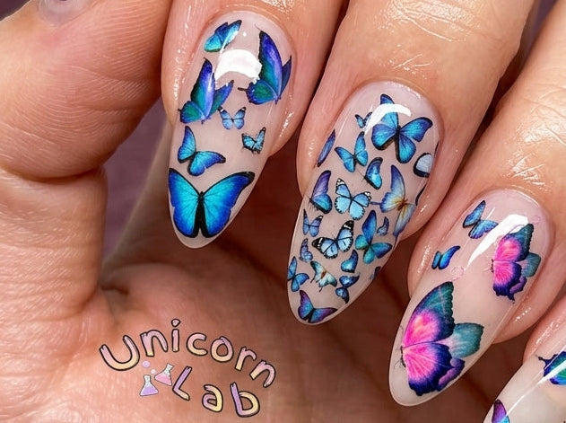 Nails with butterfly design held by a hand, with 'Unicorn Lad' branding.