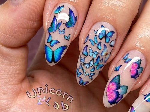 Nails with butterfly design held by a hand, with 'Unicorn Lad' branding.