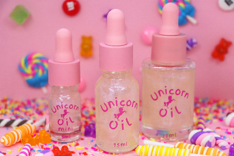 Three bottles of 'Unicorn Oil' with pink droppers on a colorful candy-themed background. - Australian made scented cuticle oil