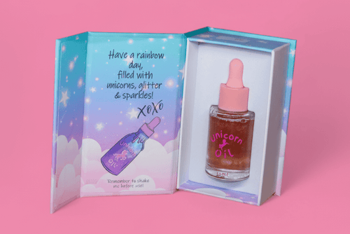 Unicorn oil bottle with dropper in a colorful box on a pink background
