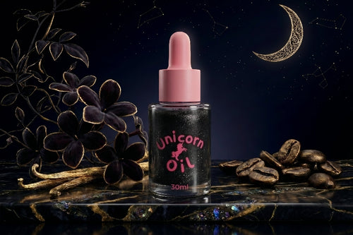 Black shimmer Unicorn Oil bottle with a pink dropper set against a starry midnight backdrop with dark florals, coffee beans, vanilla pods, and a crescent moon.