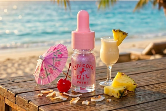 Pink bottle labeled 'Unicorn Oil Mini' on a wooden table with a tropical setting.