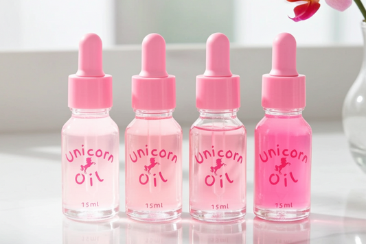Four bottles of 'Unicorn Oil' with pink droppers on a reflective surface.