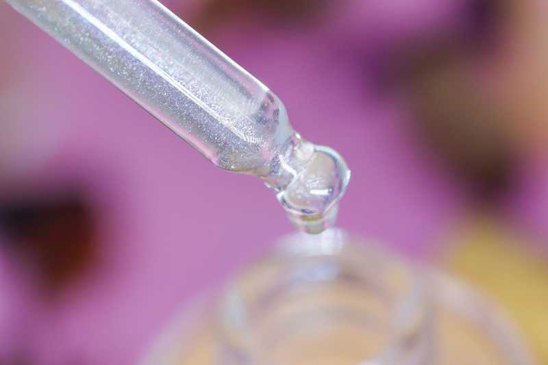 A detailed macro image of Vanilla Spice & Everything Nice Unicorn Cuticle Oil - showing off the sparkly nail oil inside dropper, dripping into a bottle